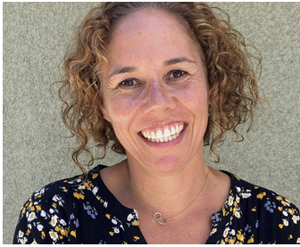 Smiling woman with curly red hair wearing a floral dress.