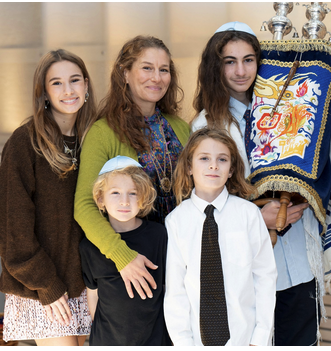 A woman with four children, standing together indoors, with one child holding a religious banner decorated with a dragon and other symbols.