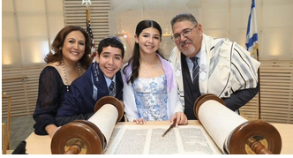 Family of four smiling at the temple, with two children and two adults, in front of the Torah scrolls.