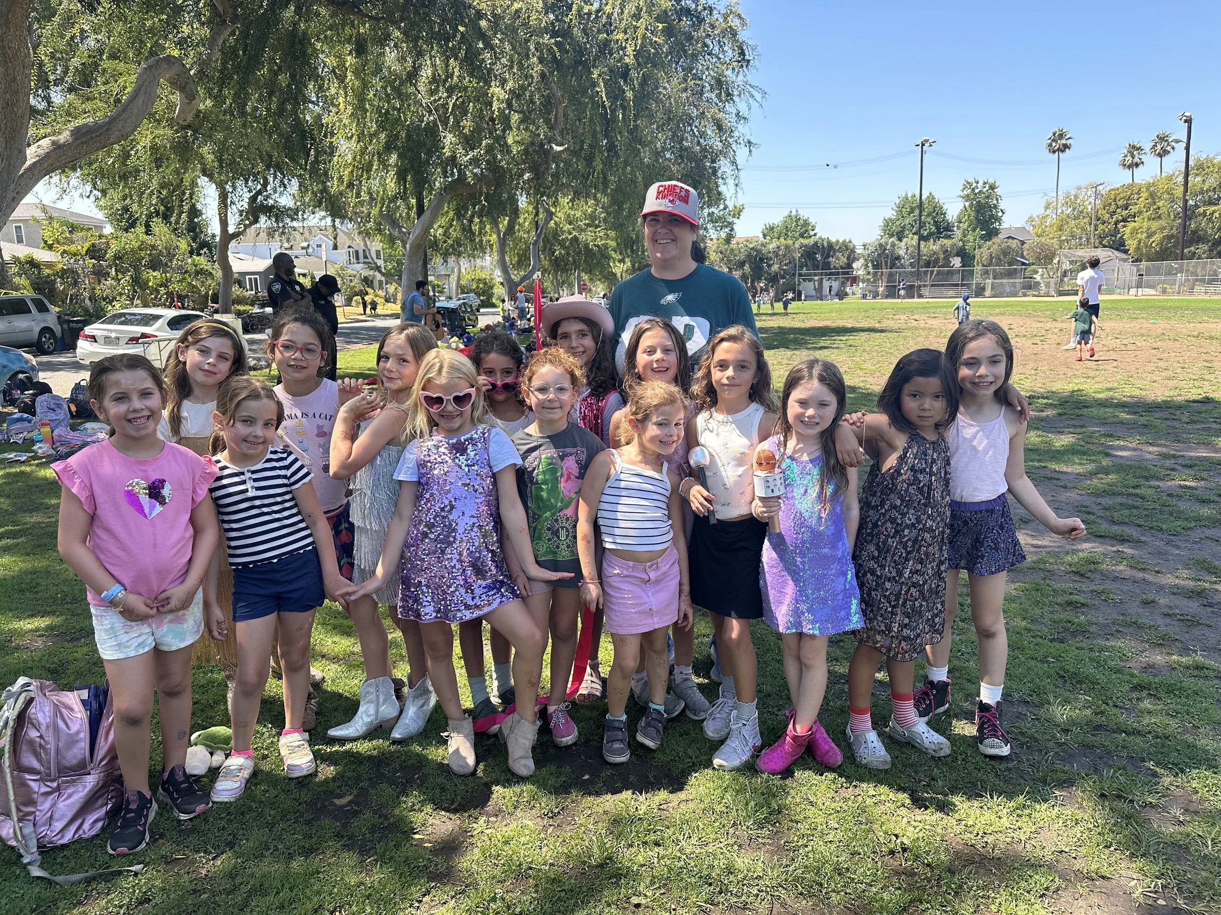 Group of young girls and one woman smiling and posing in a park on a sunny day.