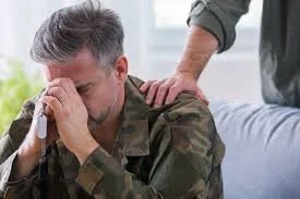 A man in military camouflage receiving a shoulder massage from another person while youg tears appear in his eyes.