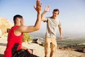 Two young men high-fiving outdoors with a scenic view in the background.