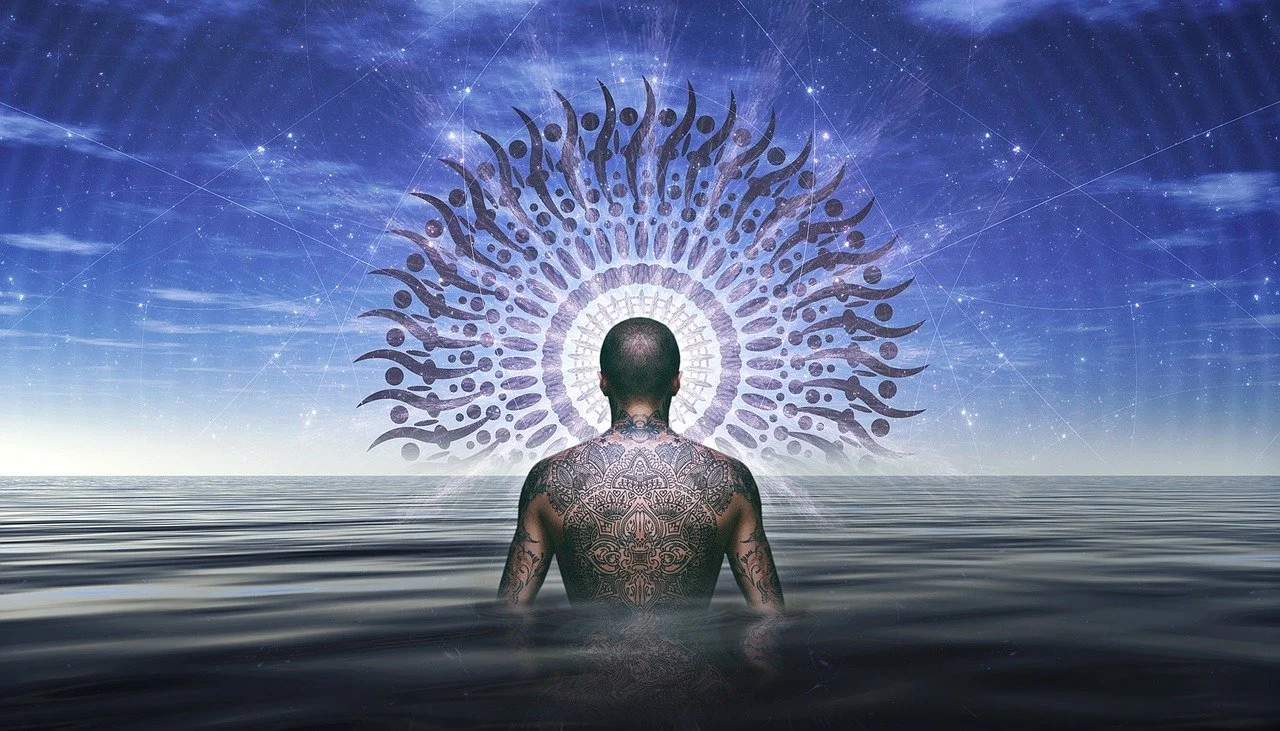 A tattooed man standing in water, facing a cosmic sky with stars, and a large abstract circular pattern with radiating designs behind him.