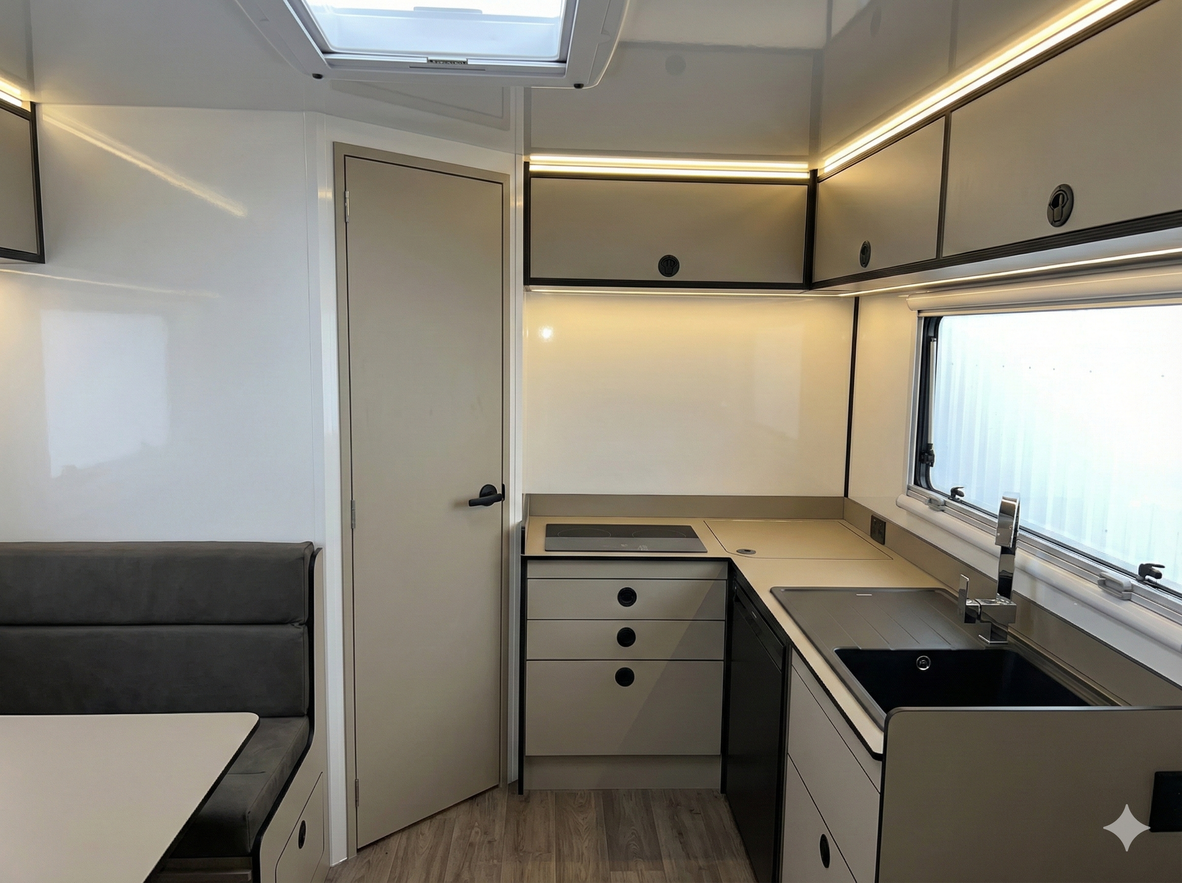 Interior of a modern camper van with white walls, gray cabinetry, a small sink, and a window, with a pack of paper towels on the counter.