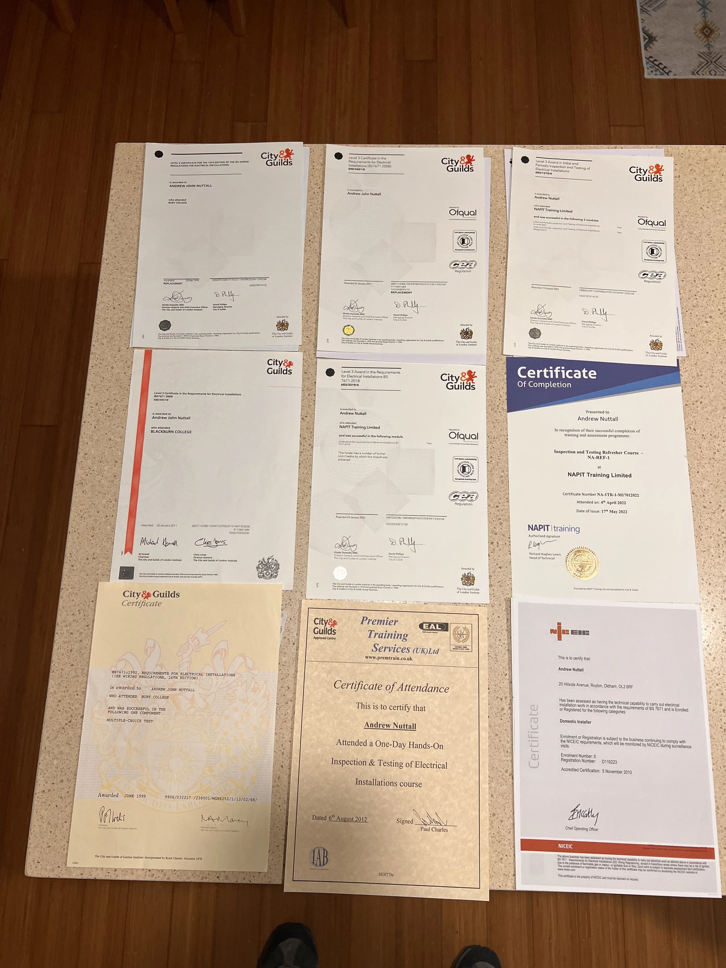 Several certificates laid out on a countertop, including electrical installation and training achievement certificates from City & Guilds, with signatures and official seals visible.