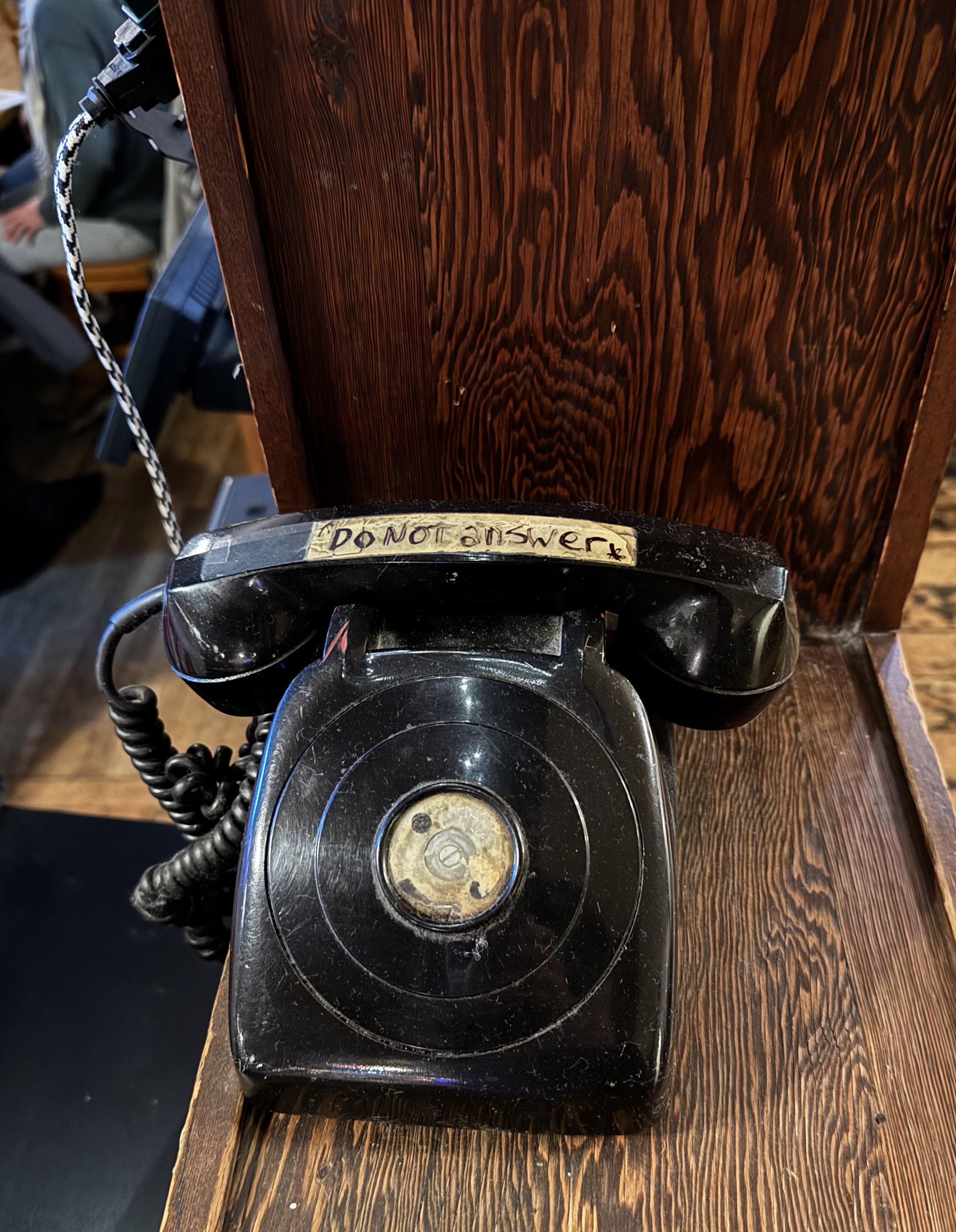 Old black rotary telephone with a handwritten note that says 'DO NOT ANSWER' on the top, placed on a wooden surface.