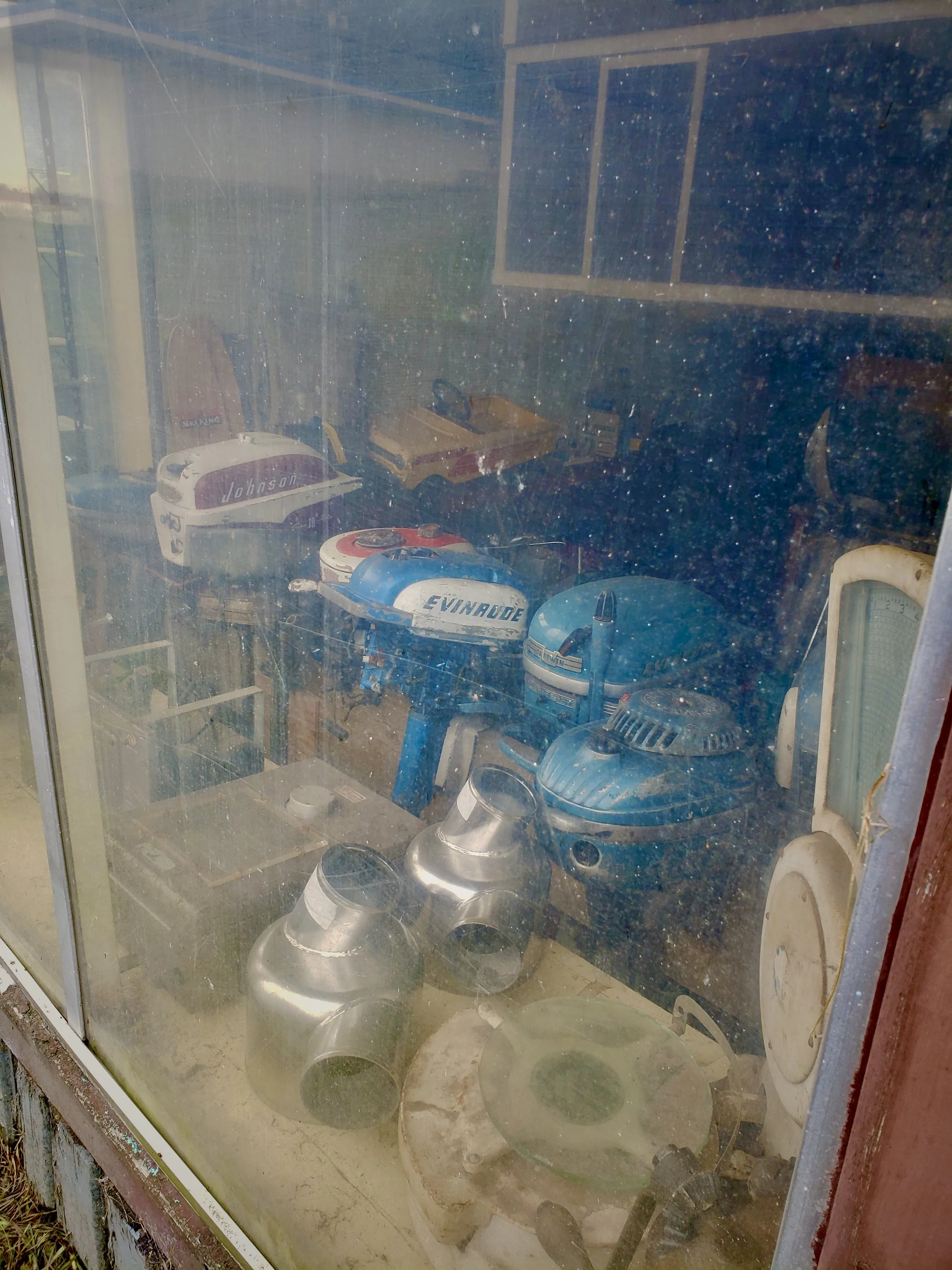 Old, dusty collection of vintage outboard motors and boat engine parts inside a glass display case.