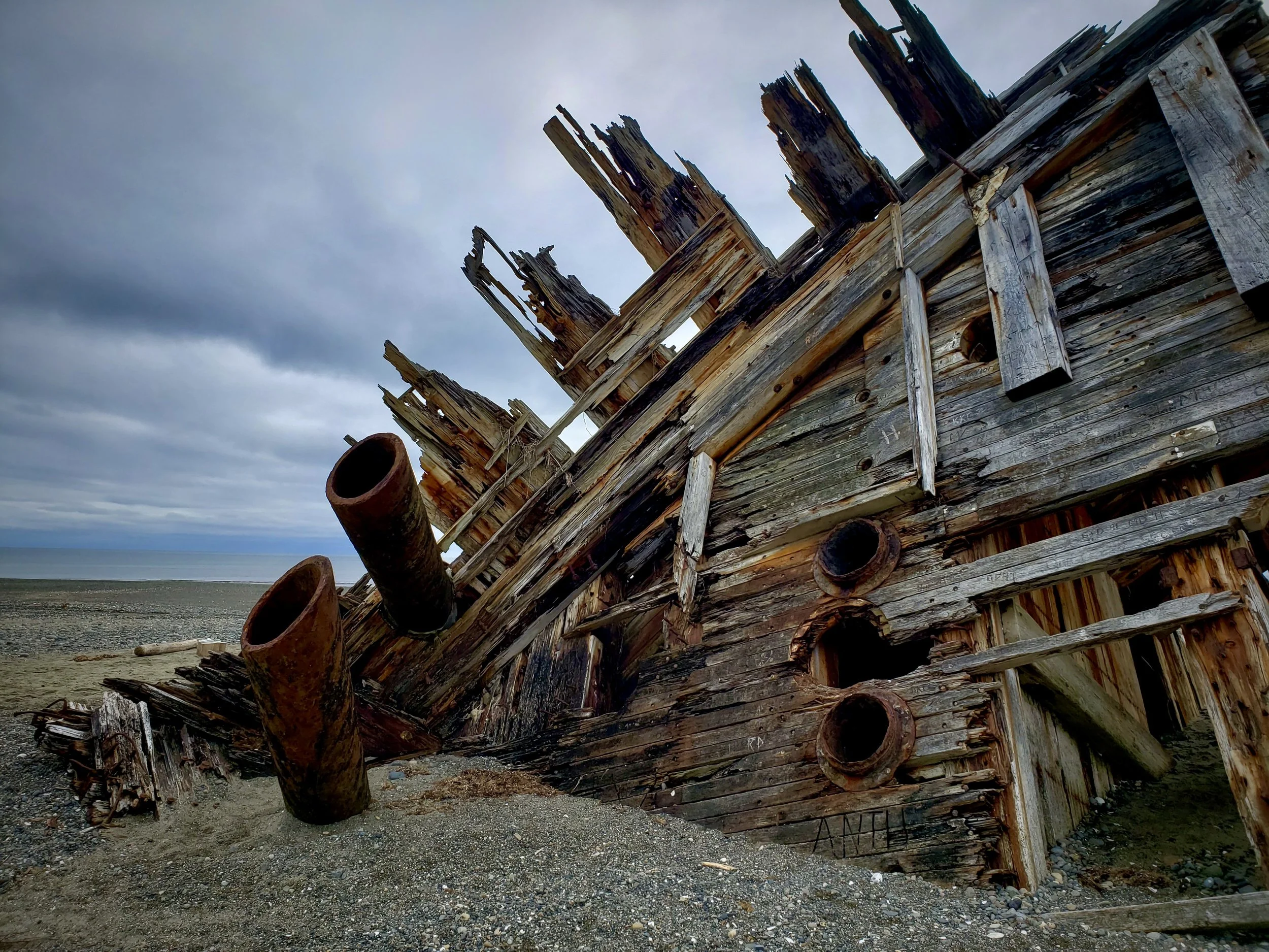 A dilapidated wooden shipwreck on a deserted beach with dark cloudy sky overhead.