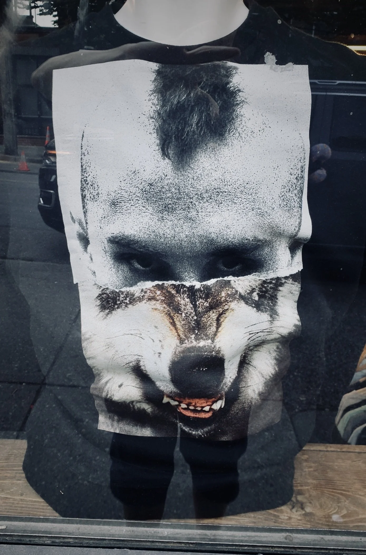 A T-shirt with a graphic design of a face merging the features of a person's face and a wolf's face, with the person's eyes above the wolf's eyes and mouth.