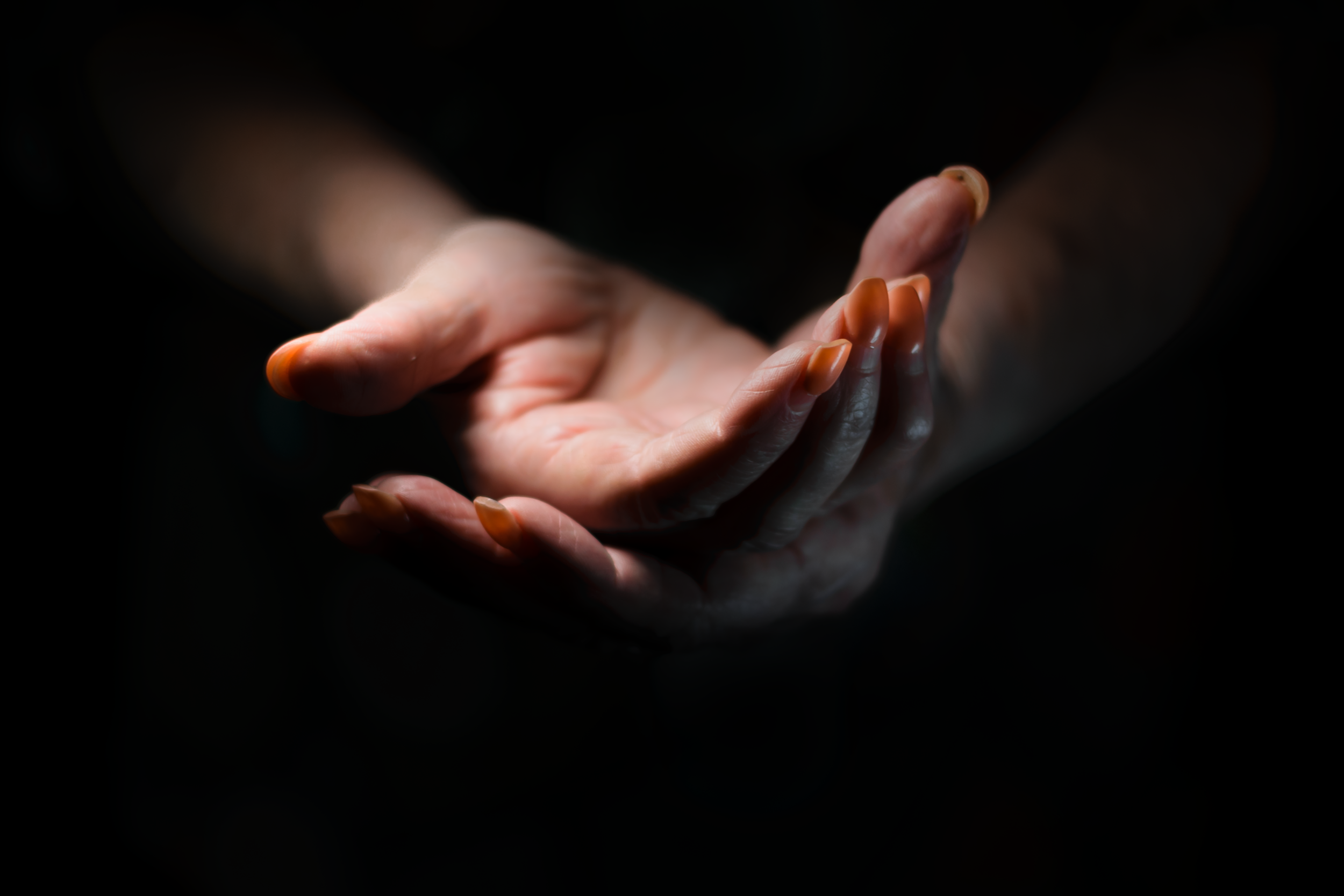 A person's hand with neatly manicured nails, held in a cupped gesture against a black background.