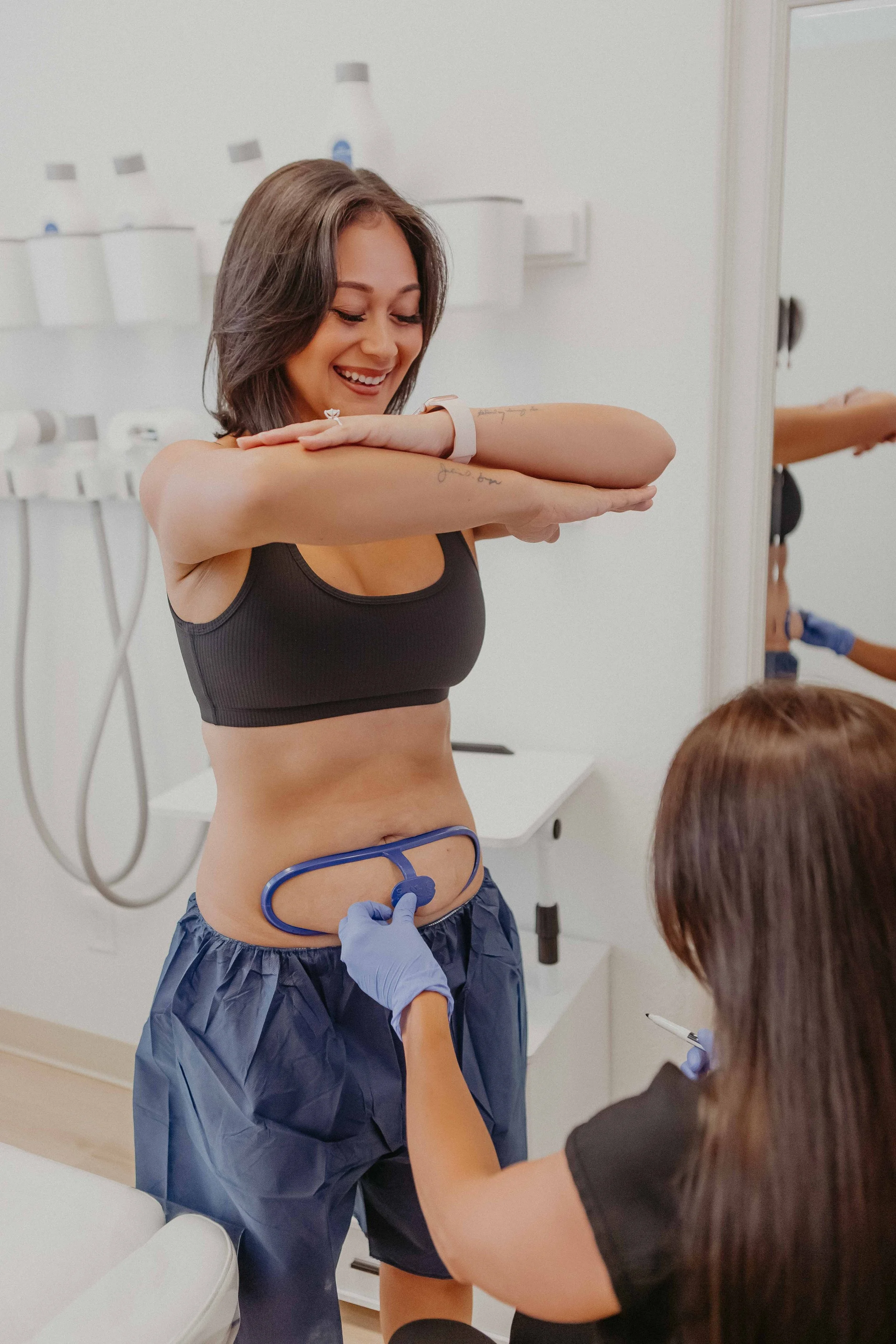 A woman at a medical checkup smiling as a healthcare professional uses a stethoscope to listen to her stomach.