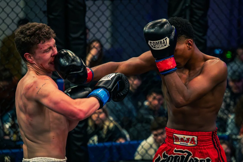 Two shirtless male fighters in a cage, one delivering a punch to the other's face during a mixed martial arts match.