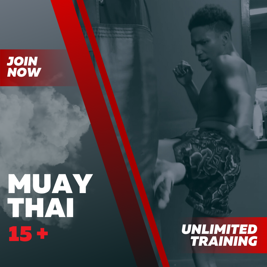 Young man in shorts practicing Muay Thai kick on a punching bag in a gym.