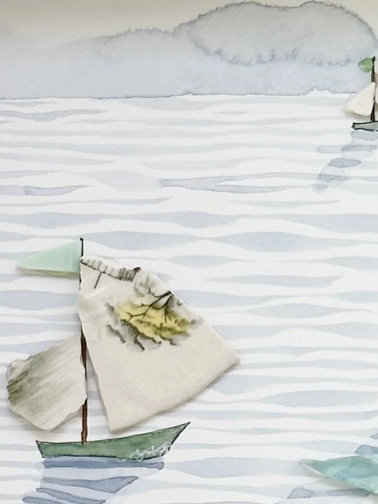 Mixed media coastal artwork with watercolour waves and sailboats made from reclaimed china shards in a white frame.