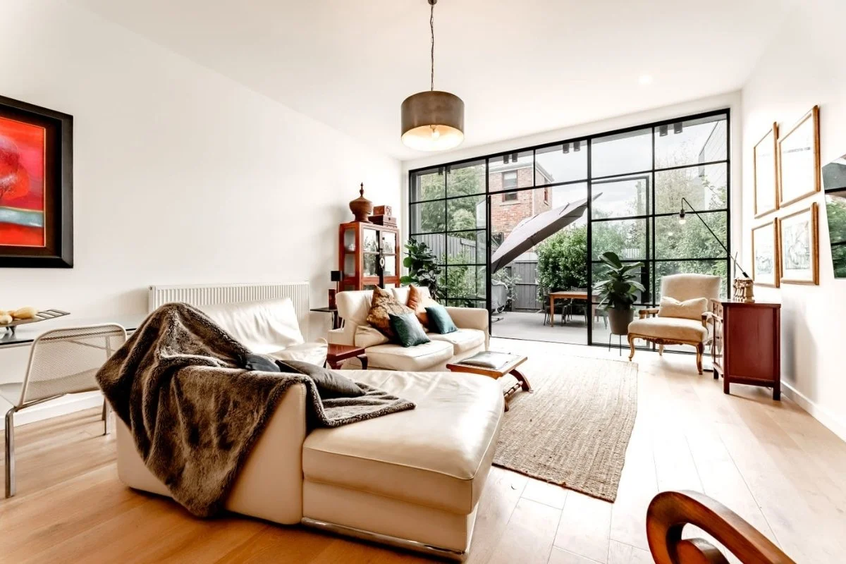 Living room with beige leather sofa, armchairs, a glass wall door leading to outdoor patio, and modern decor  by Building Evolution (Garton House).