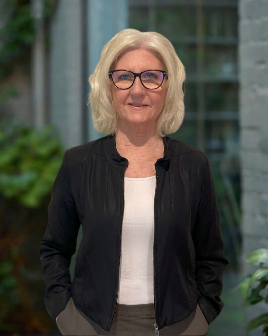 Christine Talty, Book Keeper, Building Evolution. A woman with blonde, wavy hair and black glasses stands in front of a blurred background of greenery and a modern building.