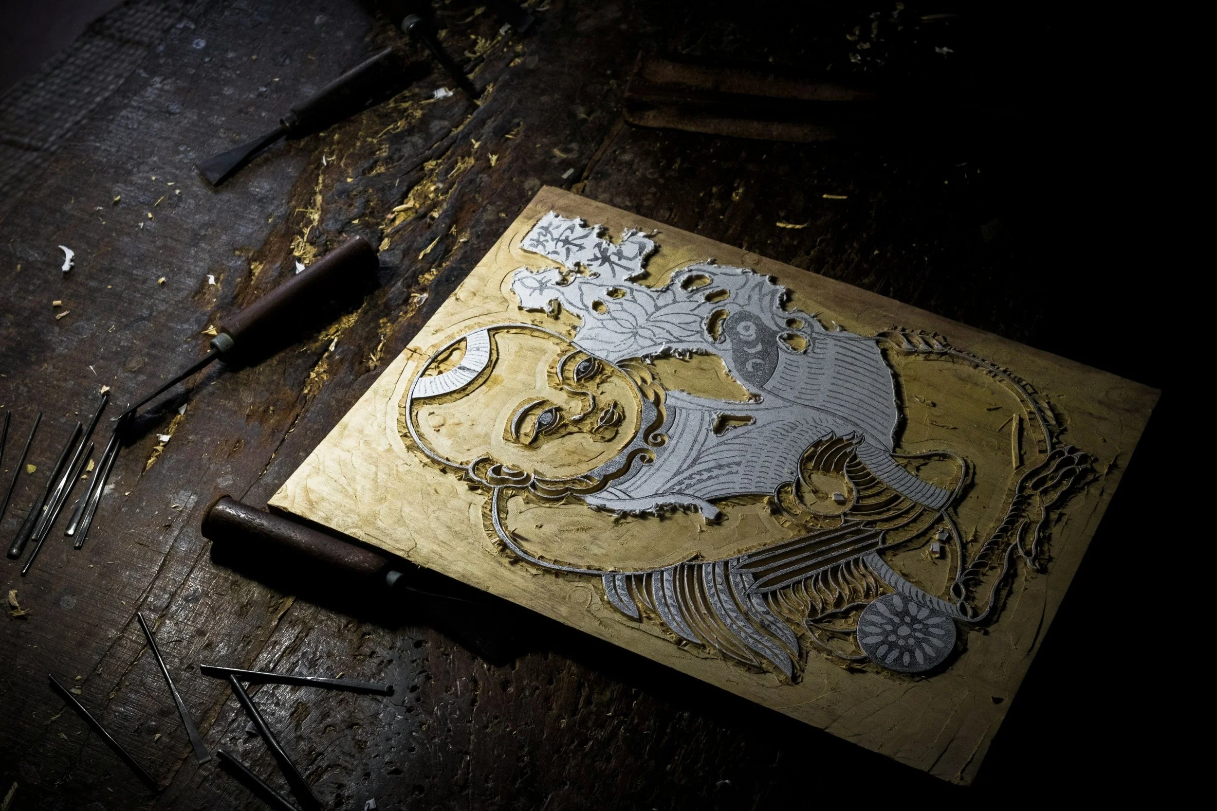 A wood carving artwork of a mythological creature on a wooden board, surrounded by carving tools and wood shavings.