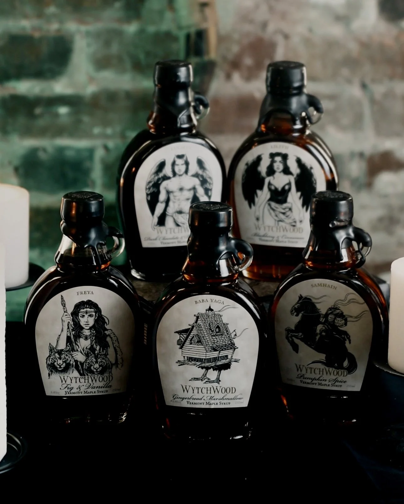 Six bottles of Wytchwood syrup with dark amber color and illustrated labels featuring fantasy characters, set against a rustic background.