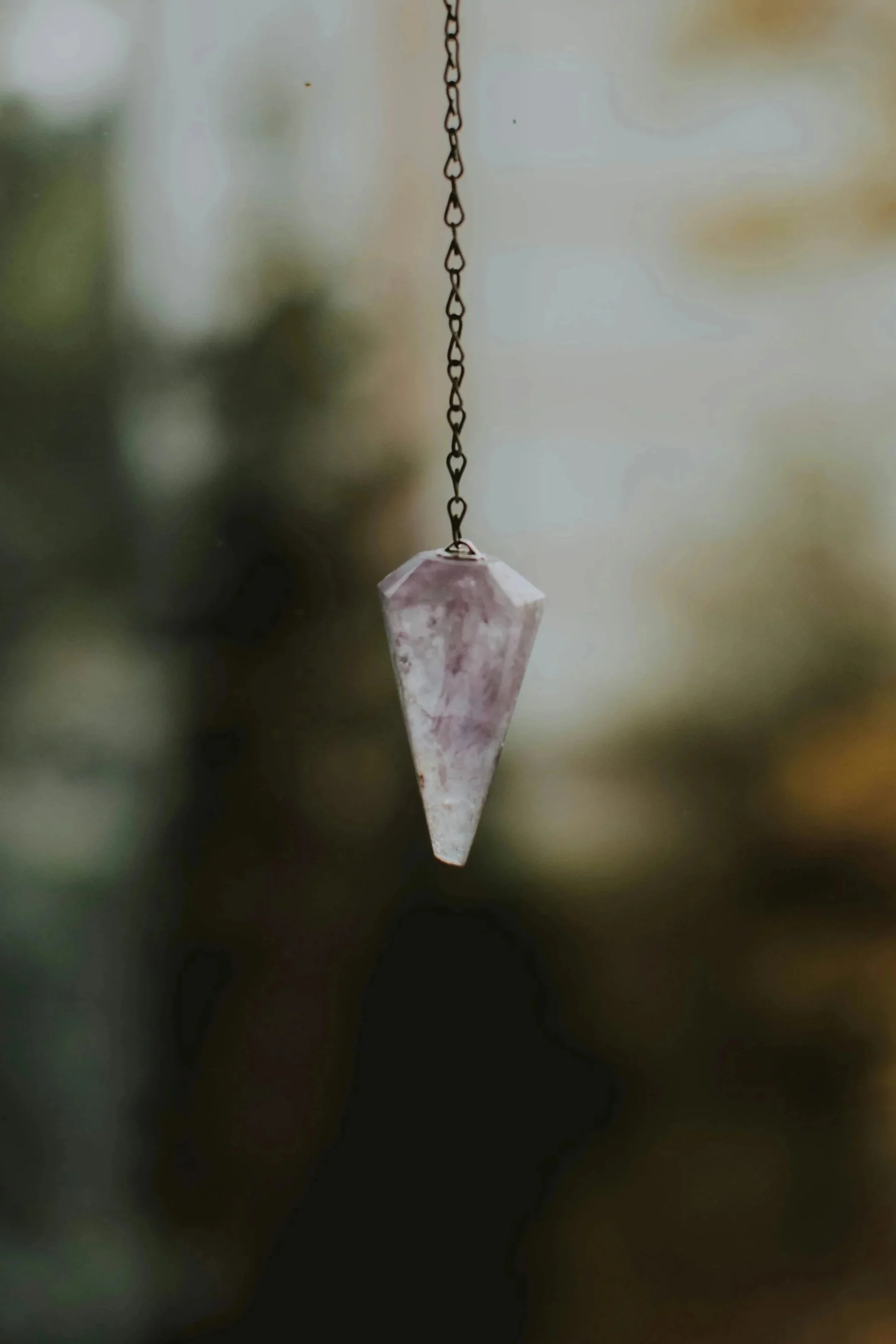 A hanging crystal pendant with a chain against a blurry outdoor background.