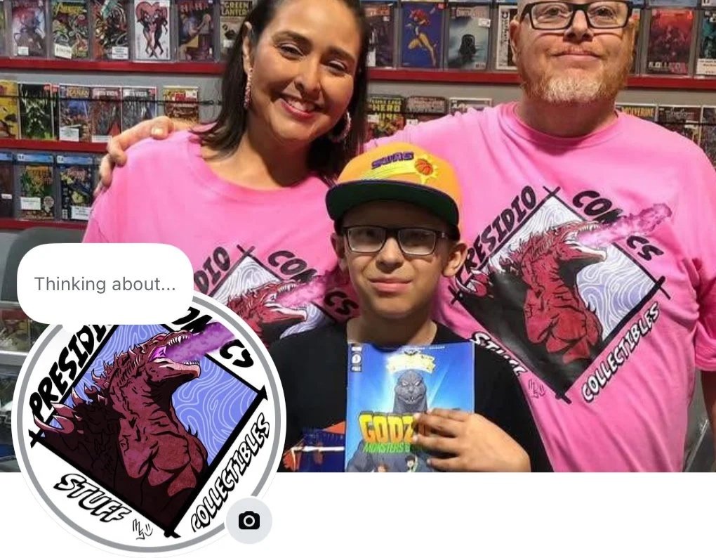 A woman and a man wearing matching pink t-shirts with a dragon logo on the front, standing behind a young boy with glasses and a yellow cap, in comic store. The boy is holding a comic book titled 'Godz.'