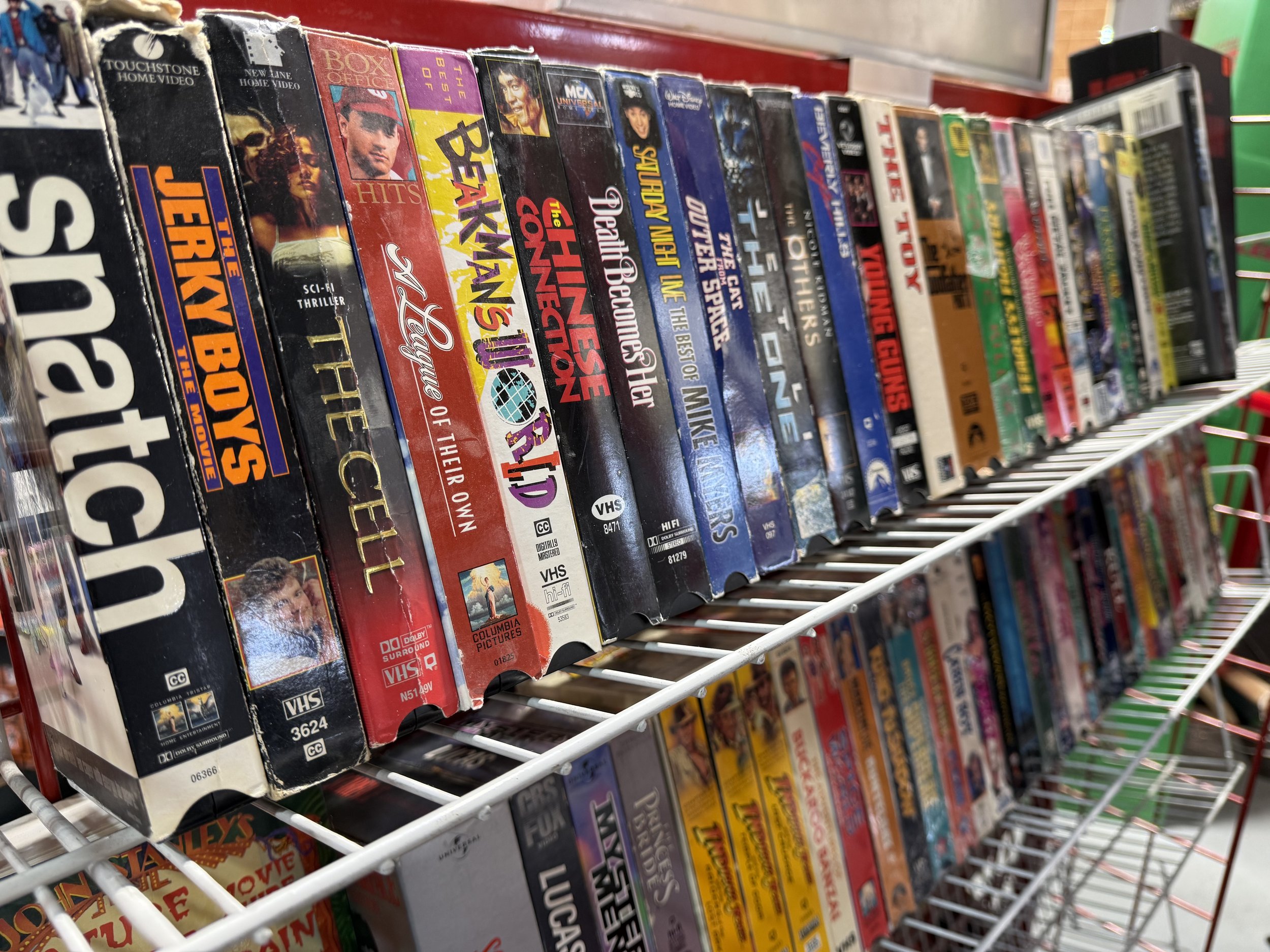 Assorted VHS tapes on a store shelf, featuring titles like 'Satanic', 'Jersey Boys', 'The Cell', and 'Beastmaster'.