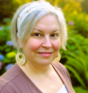 Cynthia wearing a headband, standing outdoors in a garden with green plants and flowers.