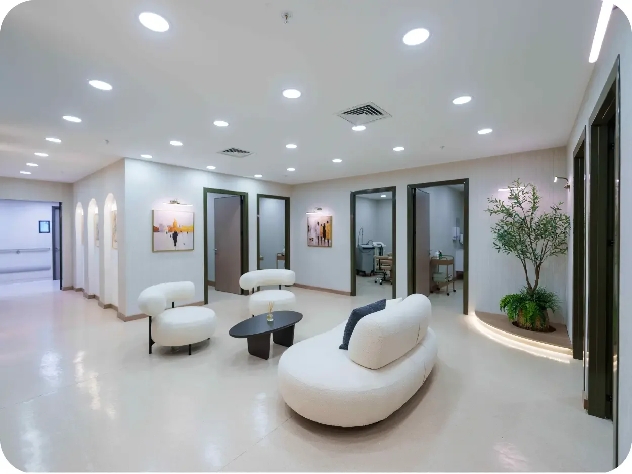 Modern hospital waiting area with white seating, small black coffee table, framed artwork on the walls, and a green potted plant.