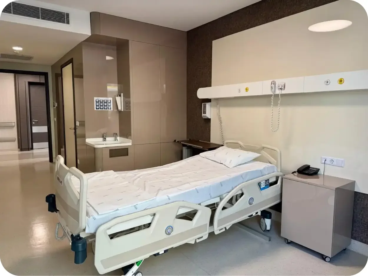 Hospital room with an empty hospital bed, bedside table, phone, and medical equipment on the wall.