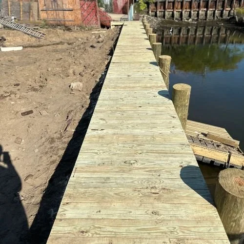 New wooden dock extending over water, with wooden posts along its sides, in a rural area.