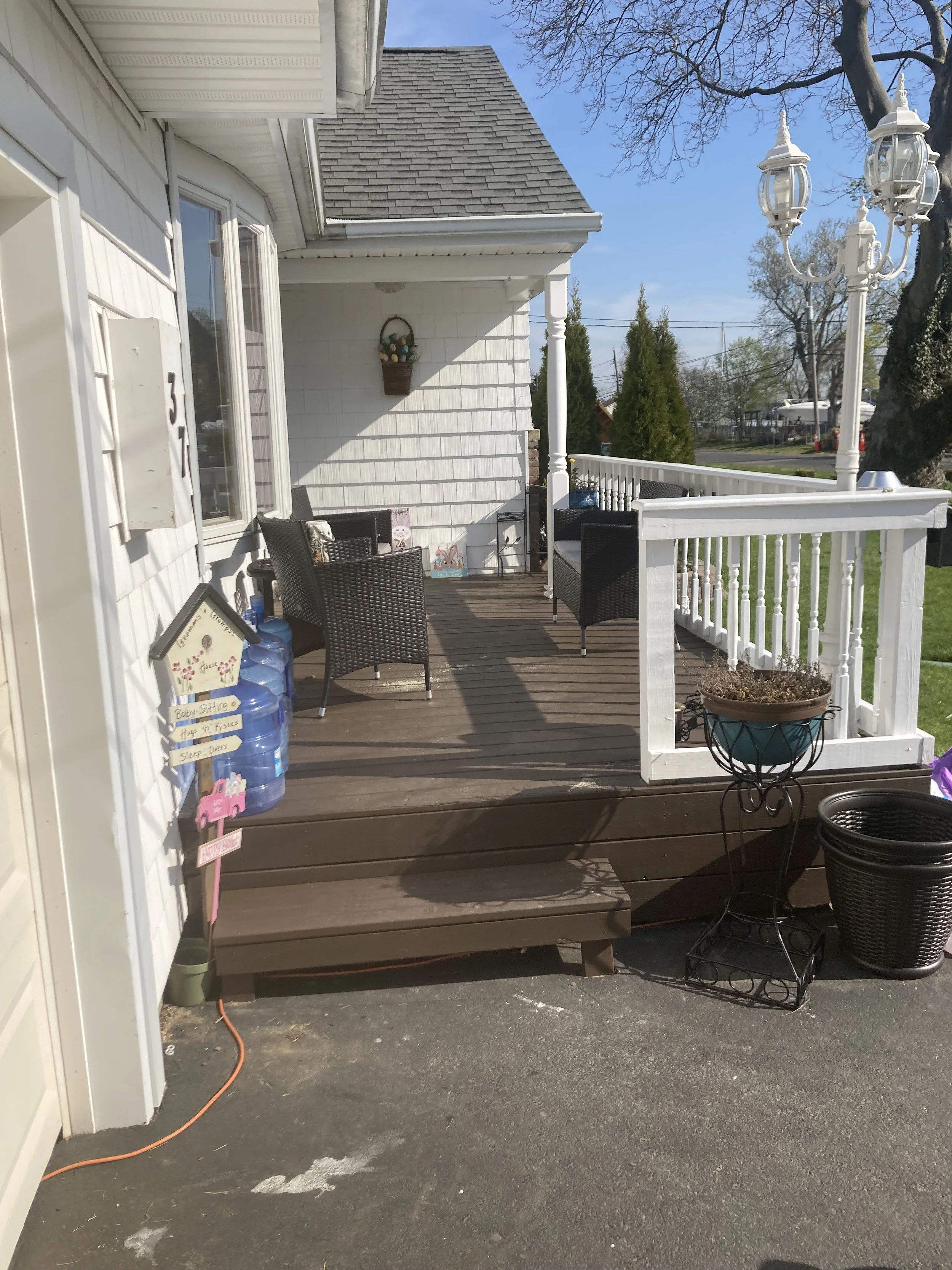 Front porch with outdoor seating area, white railing, hanging light fixture, and potted plants on a sunny day.
