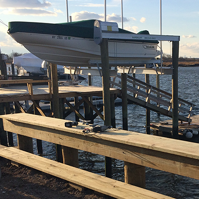 A boat on a boat lift above a body of water, with a wooden dock and tools in the foreground.