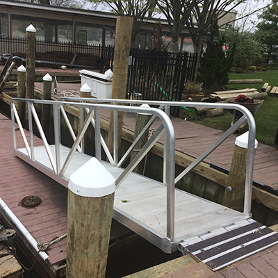Small metal dock bridge with handrails, connecting to a wooden dock on a boat slip.