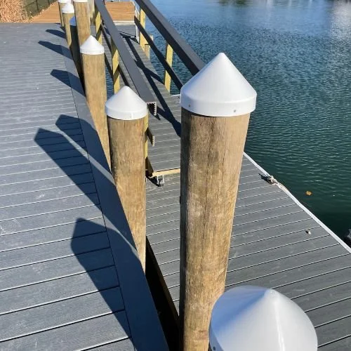 Wooden dock with white capped posts and metal railing, next to calm water.