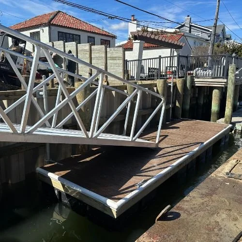 A damaged wooden dock with a fallen metal railing, partially submerged in water, located in a residential waterfront area.