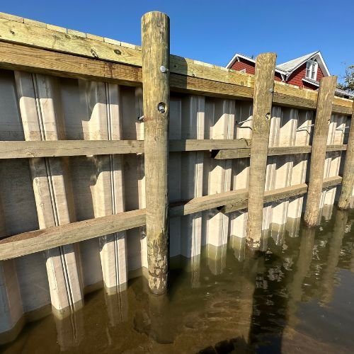 Wooden fence partially submerged in floodwater during the daytime.