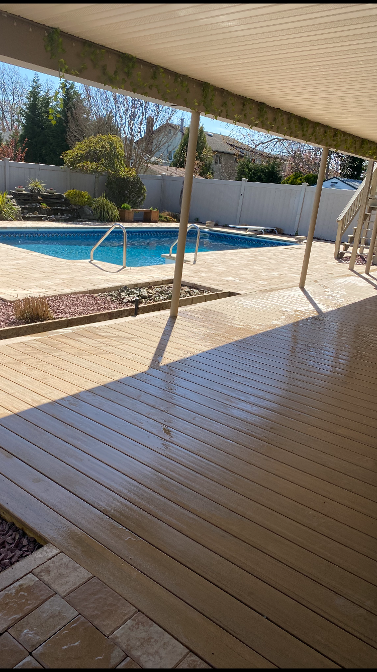 View of a backyard with a swimming pool, wooden deck, and landscaped garden enclosed by a white fence.
