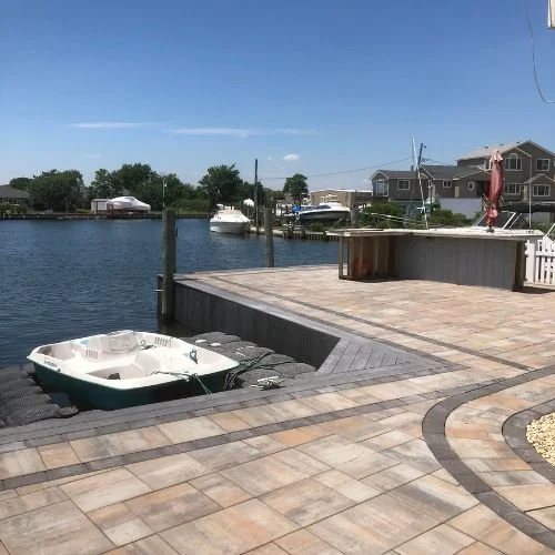View of a waterfront dock with a small boat, docked near a modern residential area with boats and a clear blue sky.