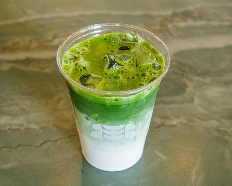 Iced matcha layered over milk in an authentic RIKYŪ cup on the café’s green stone counter.