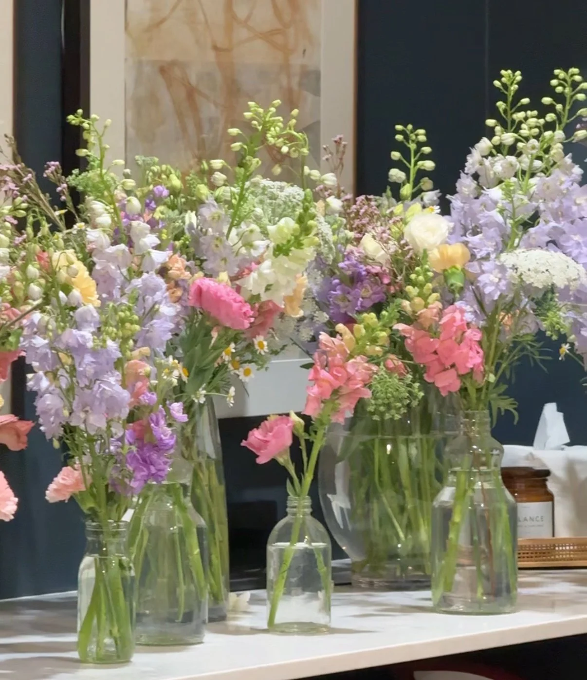 Arrangement of various pastel-colored flowers in glass vases on a white surface.