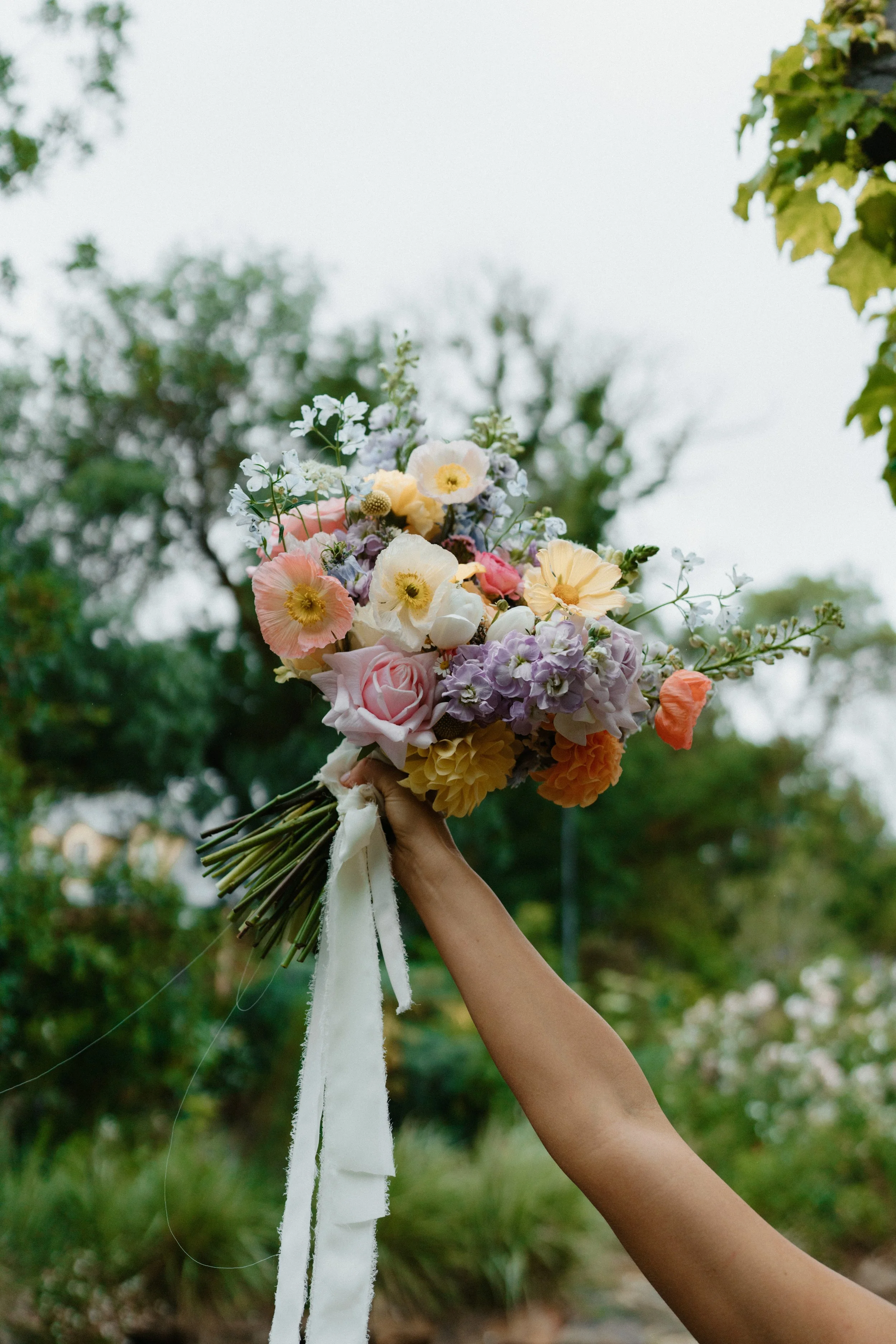 A person holding a colorful bouquet of flowers outdoors.