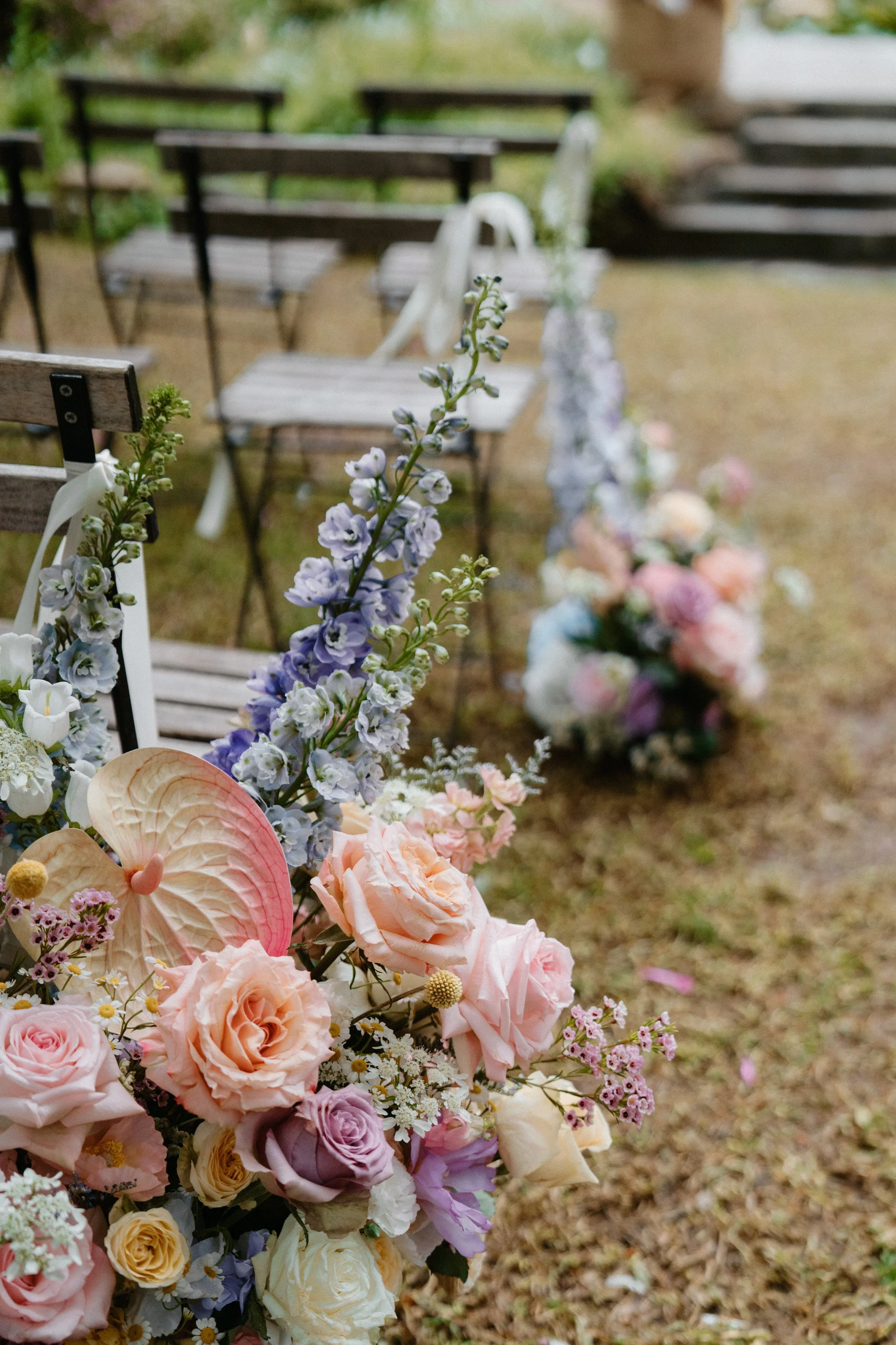 Flower arrangements and wooden chairs set up outdoors for a wedding or special event.