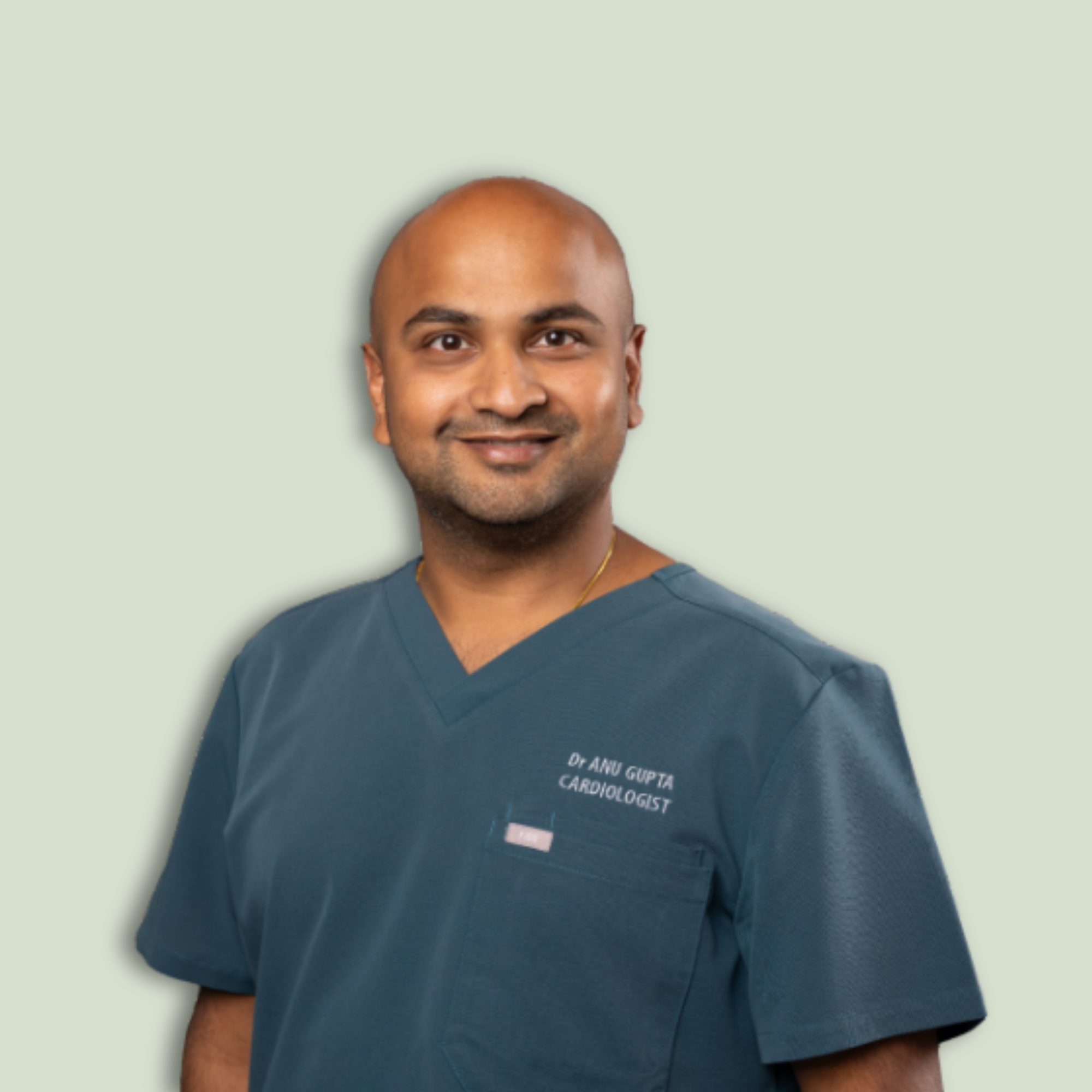 A male cardiologist in navy scrubs smiling against a light green background.