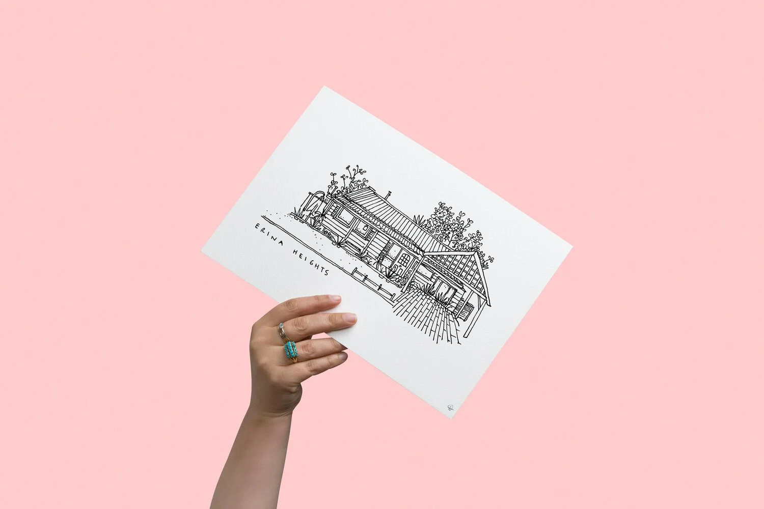 A hand holding a black line drawing of a house against a pink background. The drawing includes trees, a porch, and the text 'ERINA HEIGHTS' written on the ground.