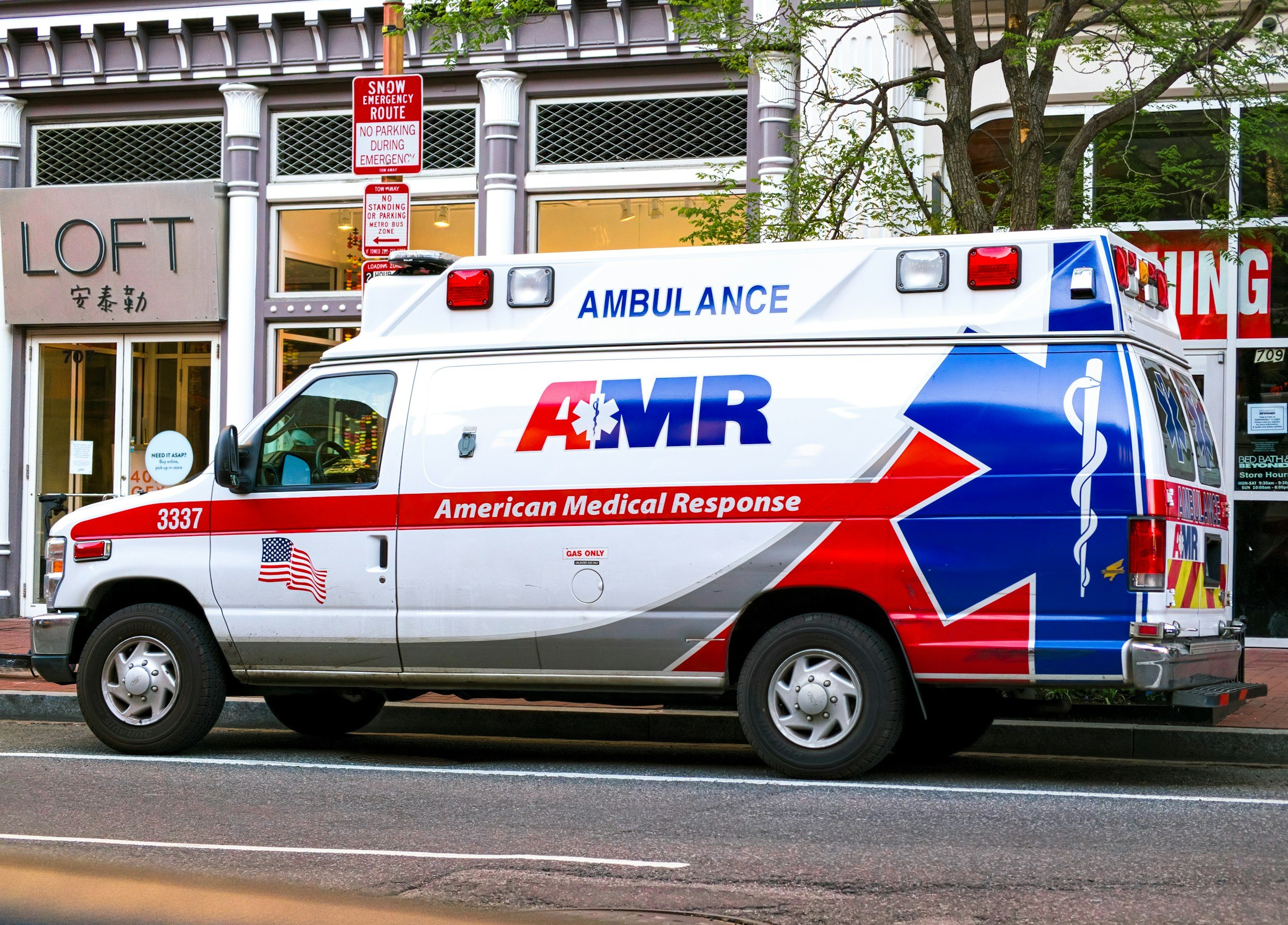 A white ambulance with red and blue markings parked on a city street.