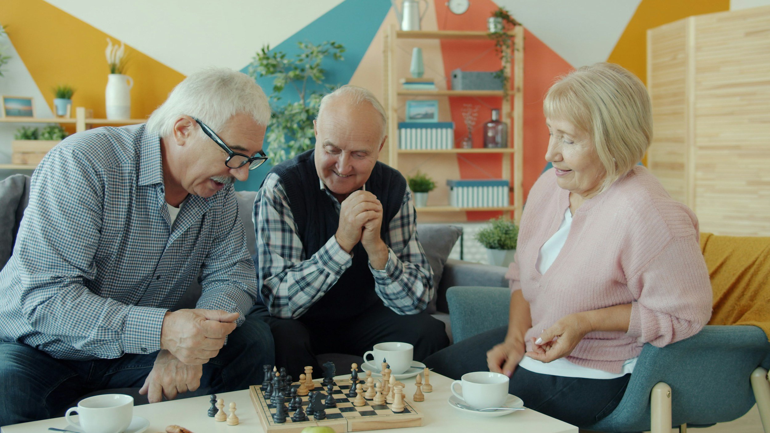Three elderly people playing chess together in a colorful, cozy room, enjoying the game and each other's company.
