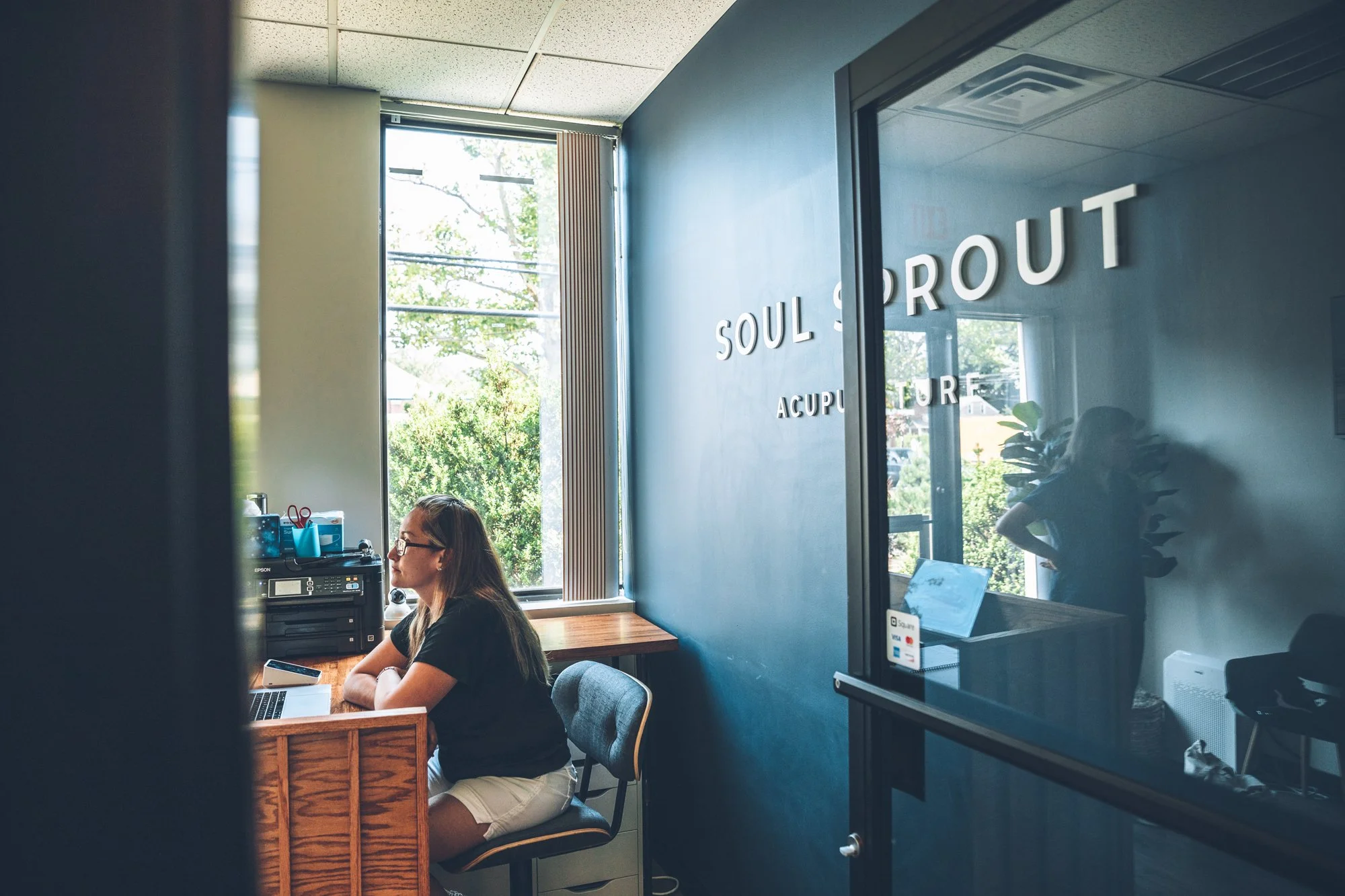 Studio manager assisting a patient at the front desk with Soul Sprout signage in the background.