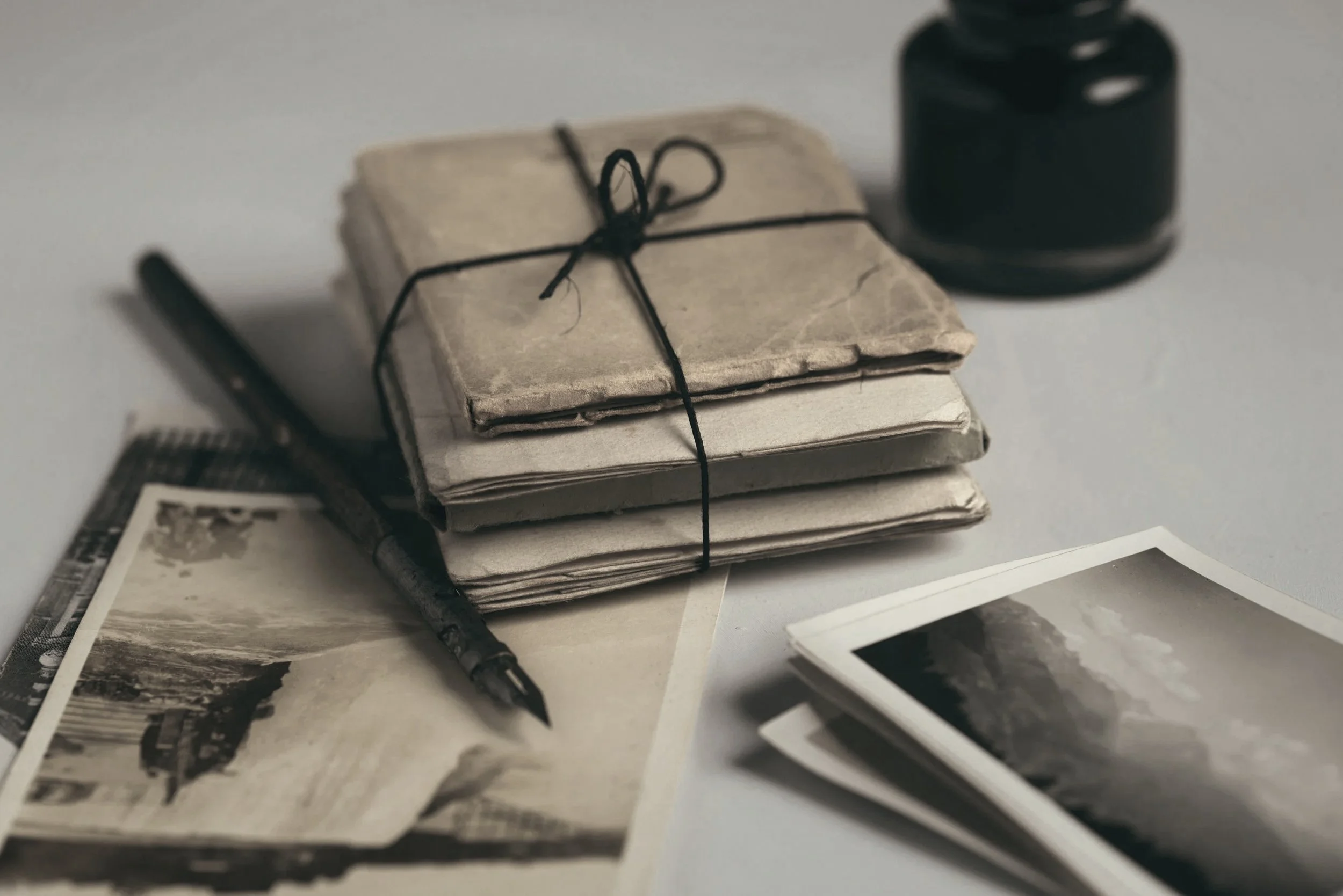 A stack of newspapers tied with black string, a black pen, photographs, and a black ink pad on a white surface.