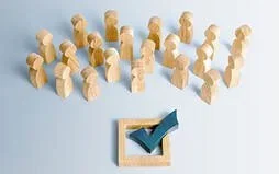 Wooden figures representing a group, with a checkmark on a sign indicating approval or completion.