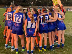 Girls' soccer team huddled together on a field before a game.
