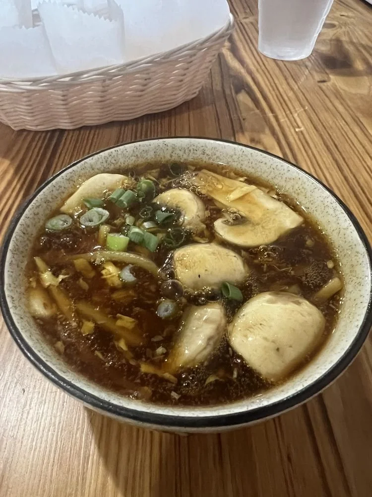 Bowl of hot soup with chicken and green onions on a wooden table.